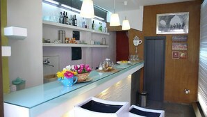 A modern kitchen with a glass countertop, shelves with bottles, a coffee machine, and a framed picture on the wall. - Antica Dimora San Girolamo (Licata)