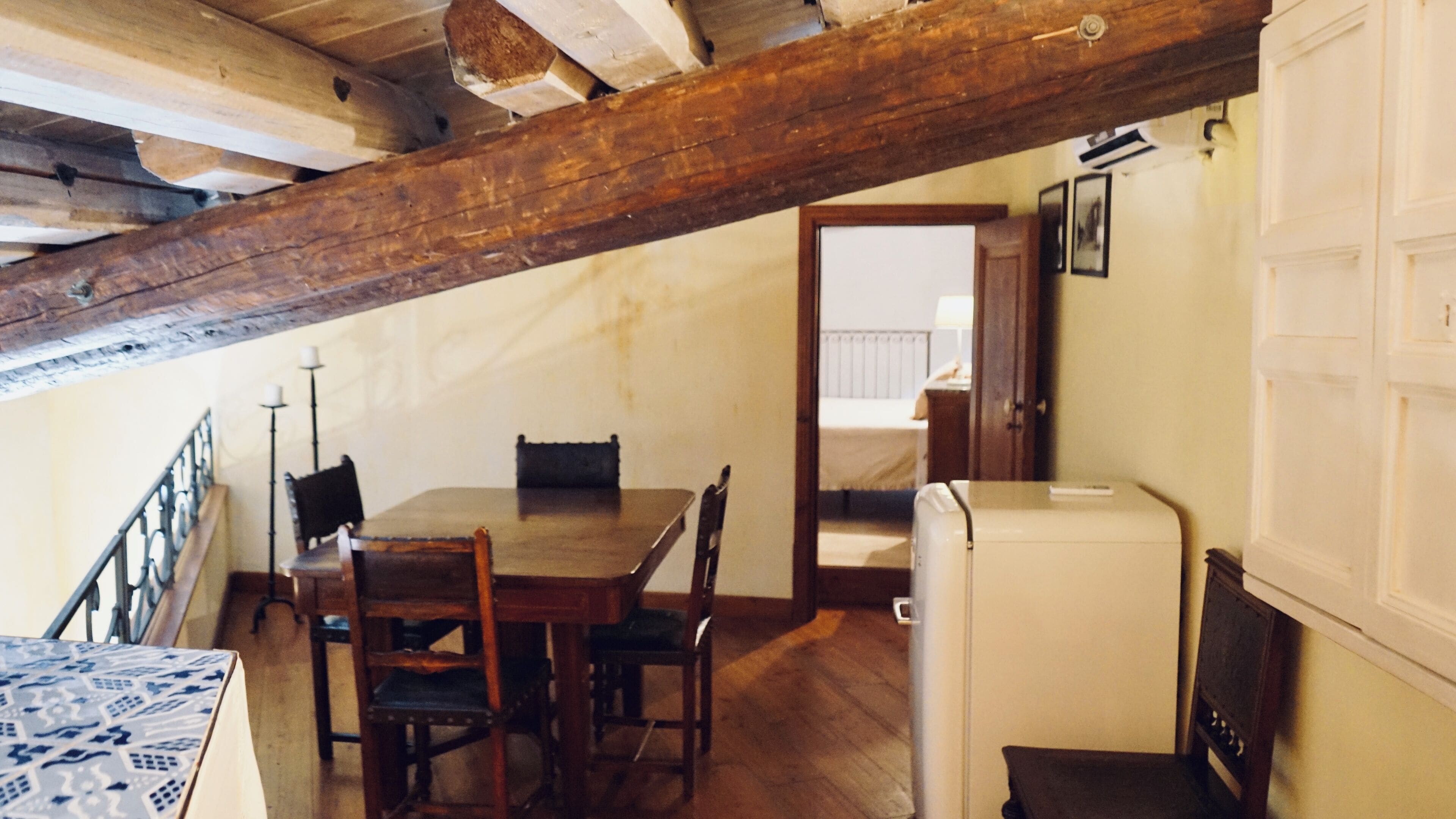 Una habitación rústica con una mesa y sillas de madera, un pequeño electrodoméstico blanco y una viga de techo de madera.