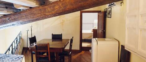 Una habitación rústica con una mesa y sillas de madera, un pequeño electrodoméstico blanco y una viga de techo de madera.