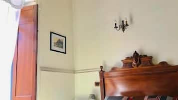 Et soveværelse med sengegavl i træ, seng med mønstret sengetøj, et natbord med en vase og en vægmonteret lampe.