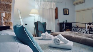 A neatly made bed with a blue pillow, a rolled towel, and a brown blanket. There is a chair and a lamp in the background. - Antica Dimora San Girolamo (Licata)