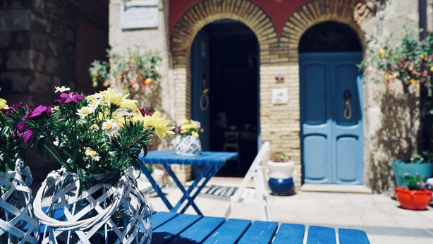 A courtyard with a blue table and chairs, a white decorative metal sculpture, and a building with blue doors and arches. - Antica Dimora San Girolamo (Licata)
