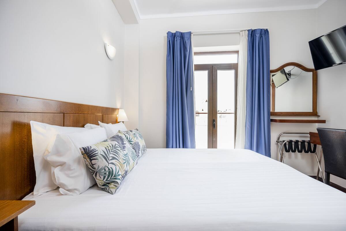 A hotel room with a bed, a nightstand, a lamp, a TV, and a window with curtains.