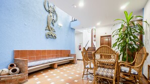 A dining area with wicker chairs and a bench, a potted plant, and a wall with a decorative fish sculpture. - Residencial Marés (Tavira)