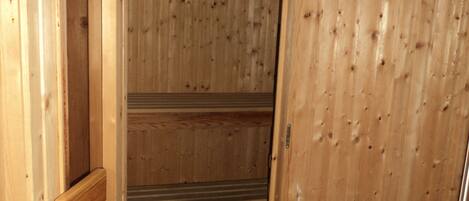 A wooden sauna with a control panel, wooden benches, and a tiled floor.