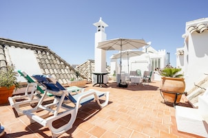 Una terraza en la azotea con sillones, una mesa y sombrillas.