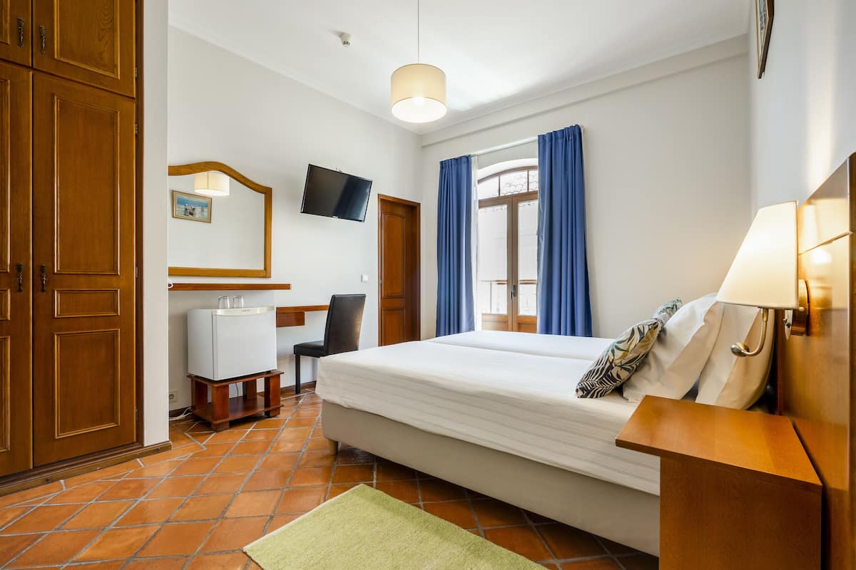 A hotel room with a bed, a desk with a chair, a television, and a window with curtains.