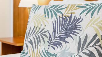 Un lit avec un drap blanc et un oreiller orné d’un motif de feuilles tropicales.