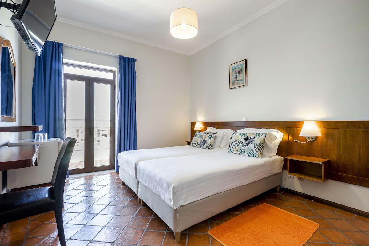 A hotel room with a bed, a desk, a chair, a TV, a lamp, and a picture on the wall.