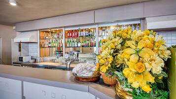 A bar area with shelves of liquor bottles, a microwave, and a floral arrangement.
