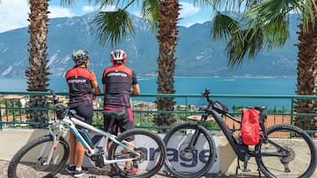Two cyclists with bicycles parked by a railing overlooking a body of water and mountains.