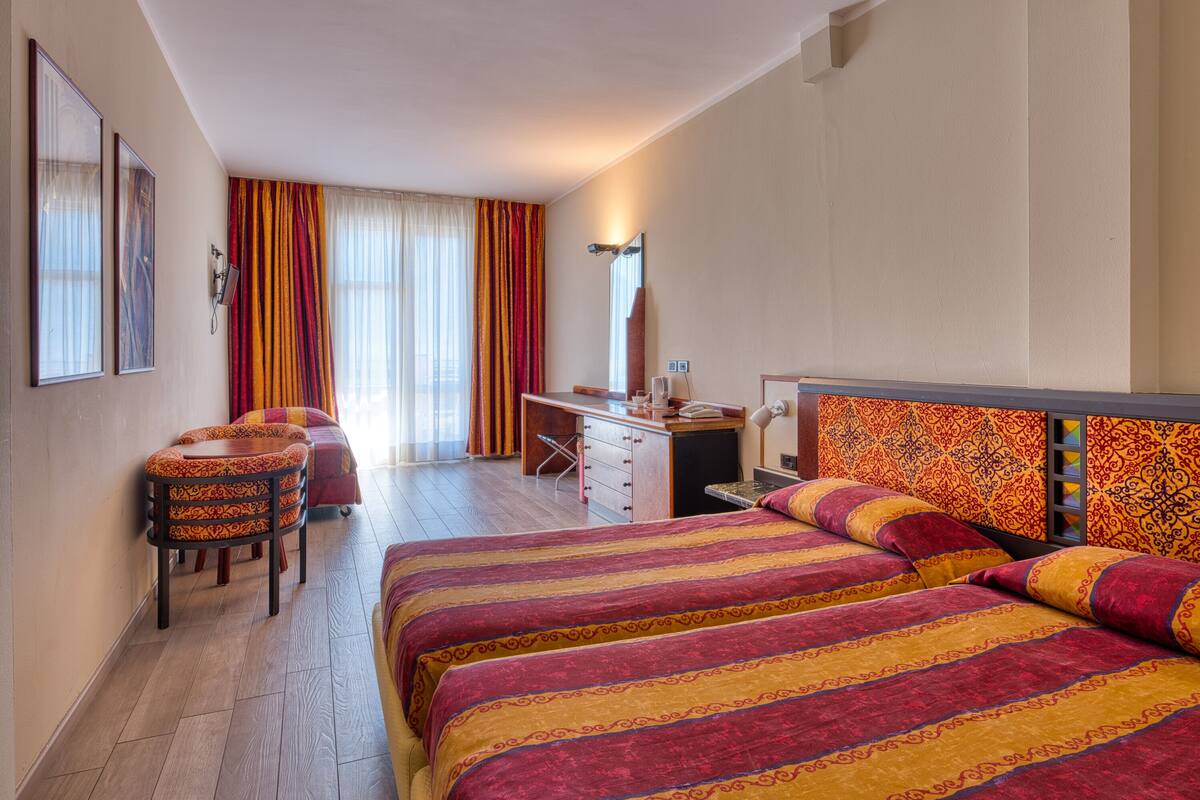 A hotel room with a large bed, a desk, a chair, and a wardrobe.
