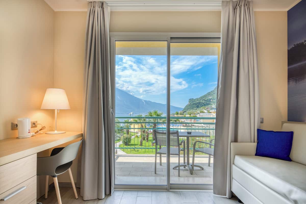 A hotel room with a balcony, a desk with a lamp, a sofa, and a view of a pool and mountains.