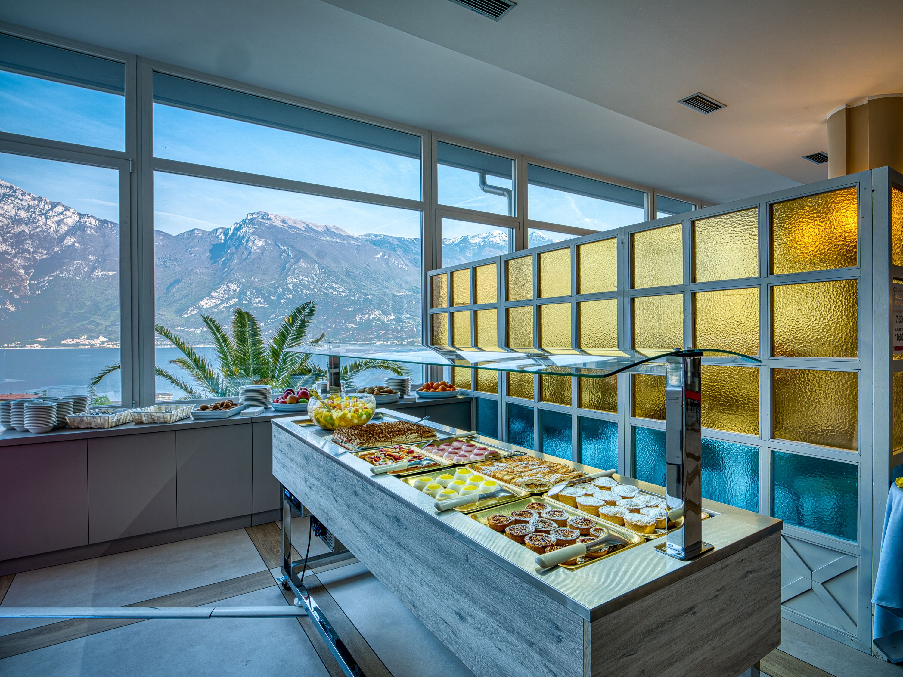 A buffet with a variety of food items, a large window with a mountain view, and a decorative glass partition.