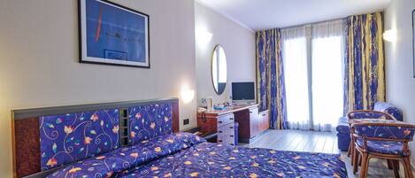 A hotel room with a bed, desk, chair, and a large window with curtains.