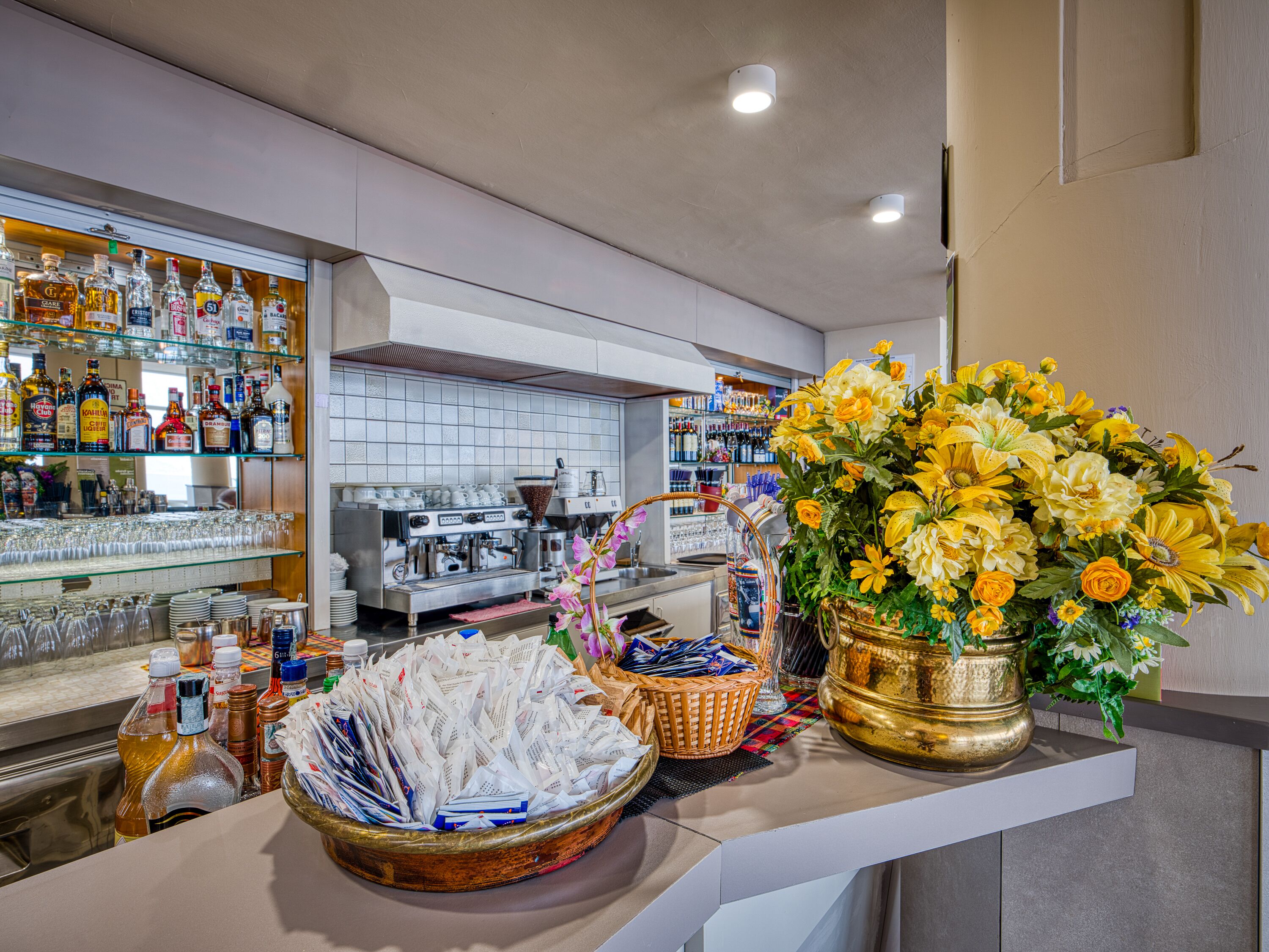 Un espace bar équipé d’une machine à café, d’une variété de bouteilles d’alcool et d’un grand arrangement floral.