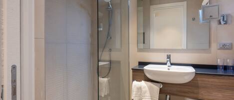 Een moderne badkamer met een douchecabine van glas, een grote spiegel en een houten wastafelmeubel.