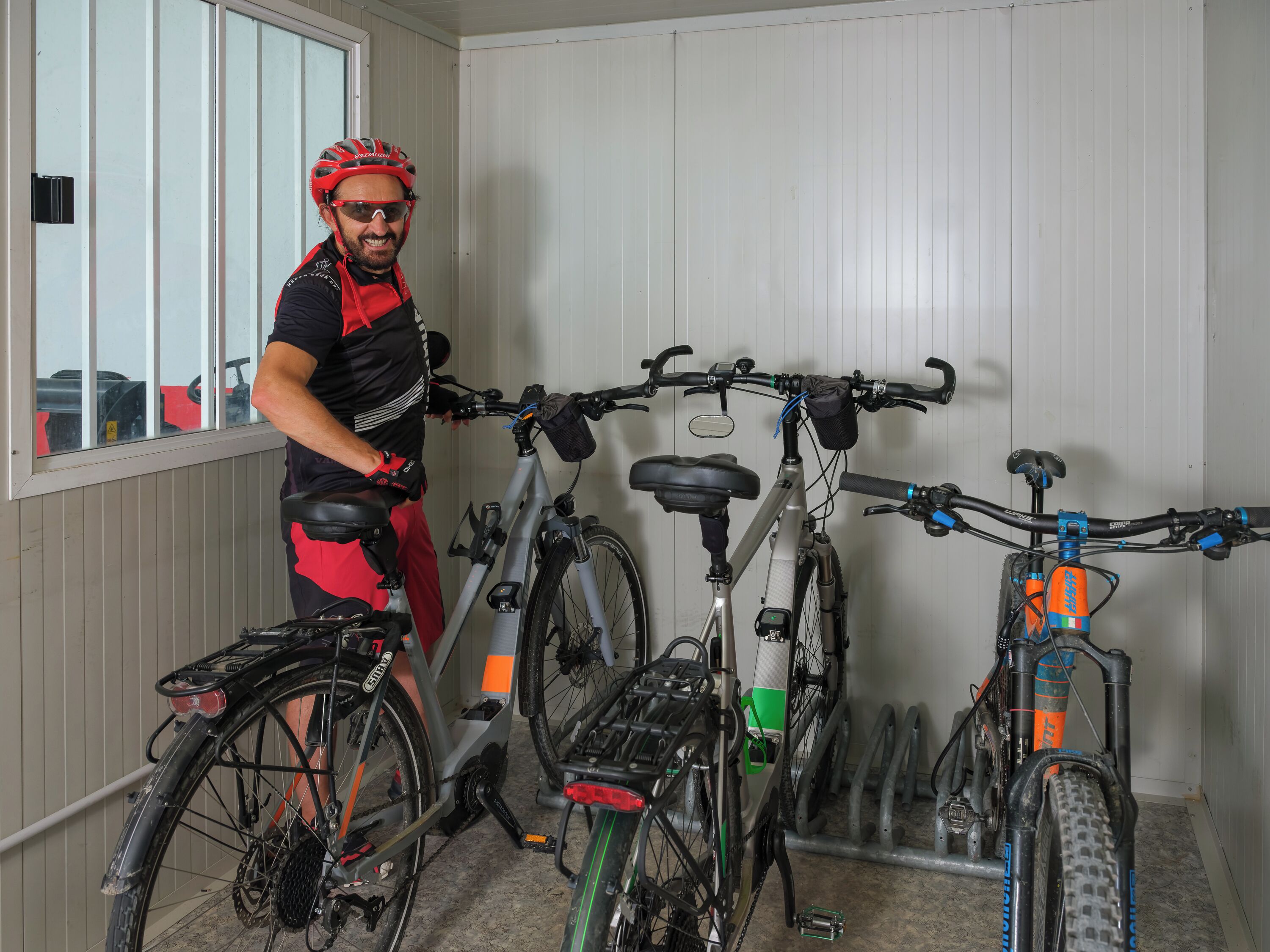A person standing next to a bicycle in a room with white walls and a window.