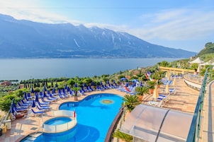 A resort pool with blue chairs and umbrellas, surrounded by mountains and a lake.