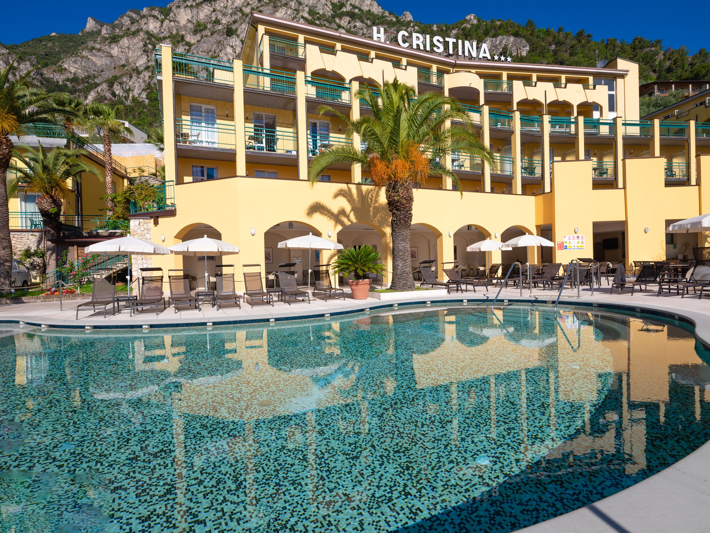 Un hotel anomenat H. Cristina amb una zona de piscina, gandules i palmeres.