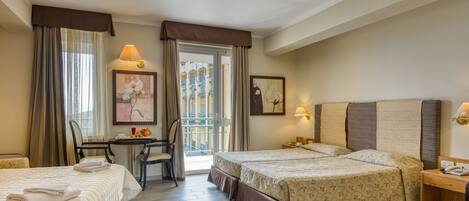 A hotel room with two beds, a desk, and a chair. There are two paintings on the walls, a window with curtains, and a balcony visible through the door.