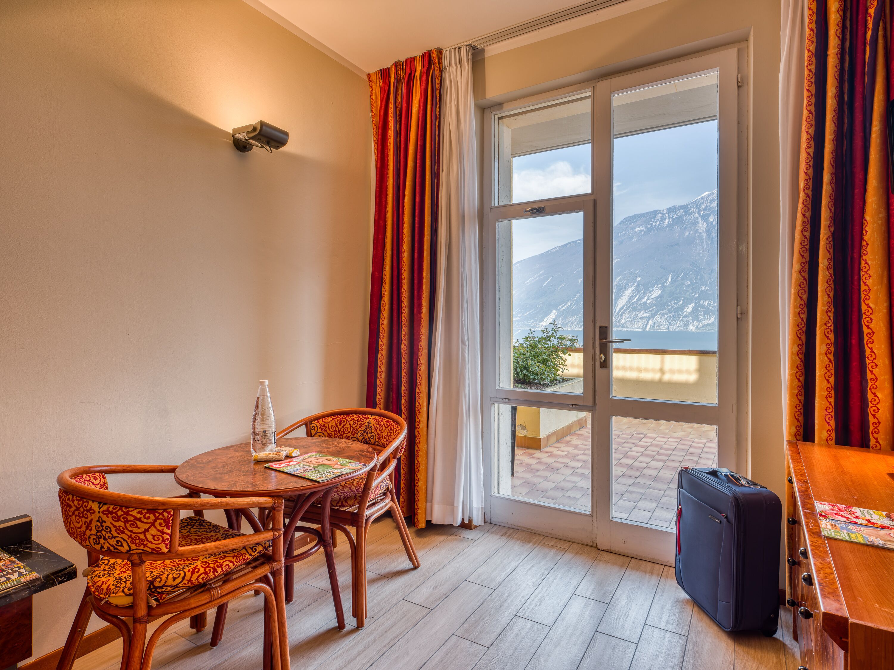 Una habitación con una mesa y sillas de madera, una maleta y vistas a montañas a través de un ventanal grande.