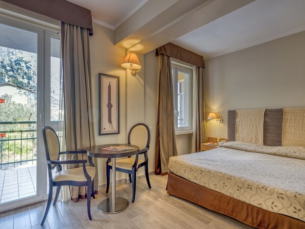 A hotel room with a bed, a table with chairs, a window with curtains, and a wall-mounted lamp. - Hotel Cristina (Limone sul Garda)