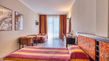Ein Hotelzimmer mit Bett, Schreibtisch, Stuhl und einem kleinen Tisch. Vorhänge und ein Fenster sind vorhanden.