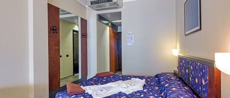 A hotel room with a large bed, an air conditioning unit, a mirror, and a framed picture on the wall.