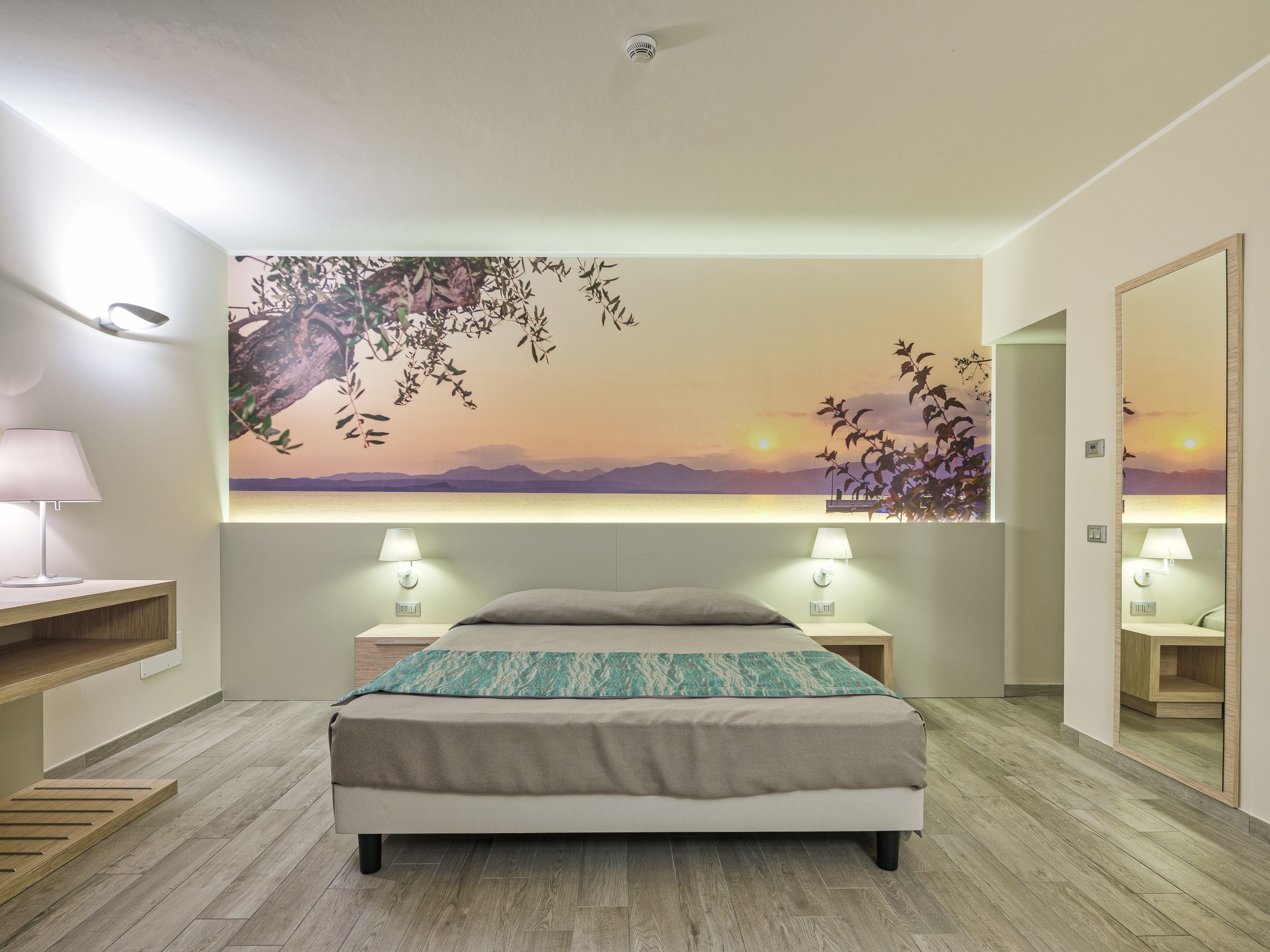 A modern bedroom with a bed, bedside lamps, a large wall mural, and a wooden floor.