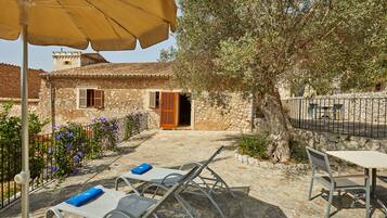 A stone building with a tiled roof, a tree, and outdoor seating with umbrellas.