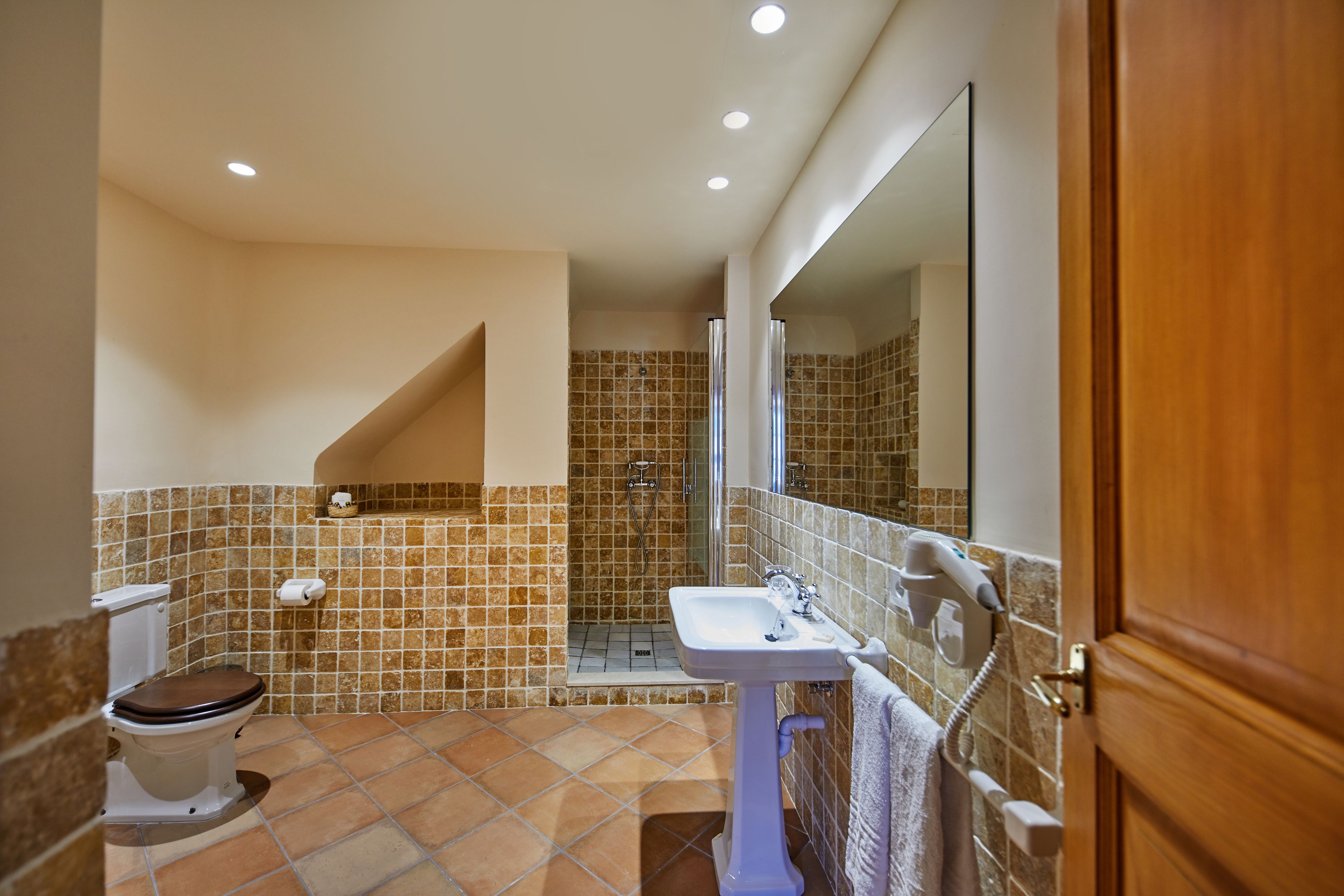 A bathroom with a toilet, sink, shower, and a mirror.