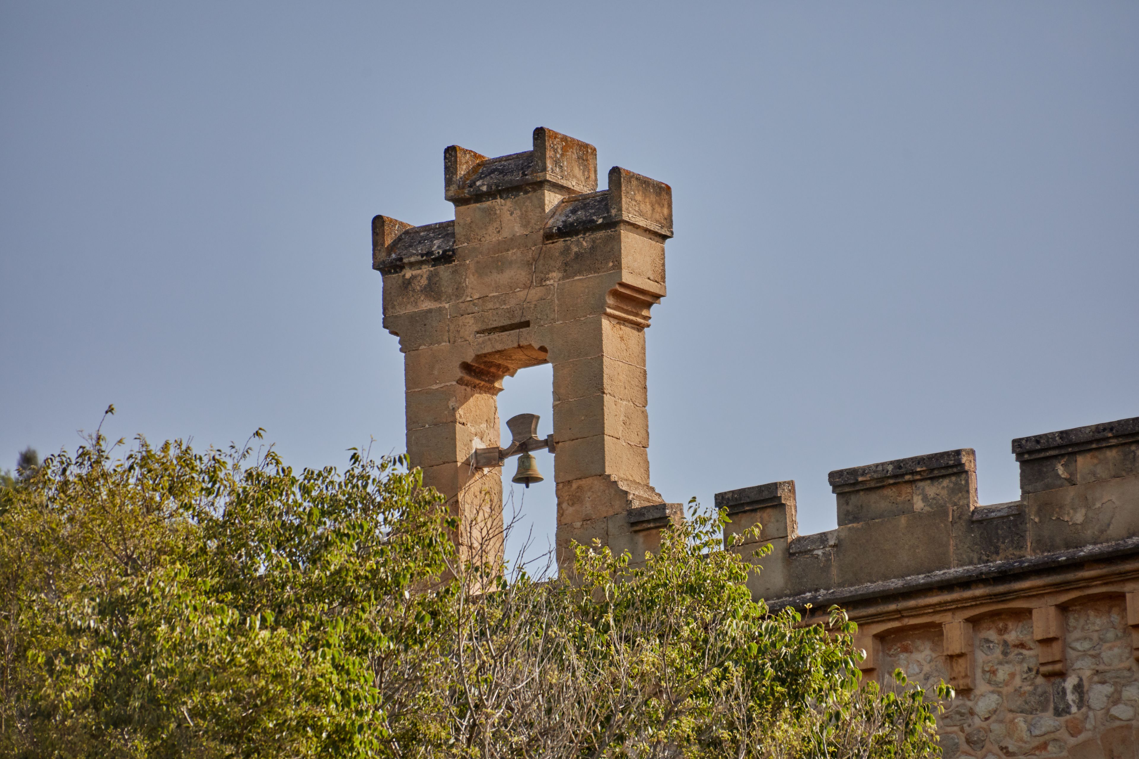 Una torre de piedra con una campana, rodeada de vegetación.