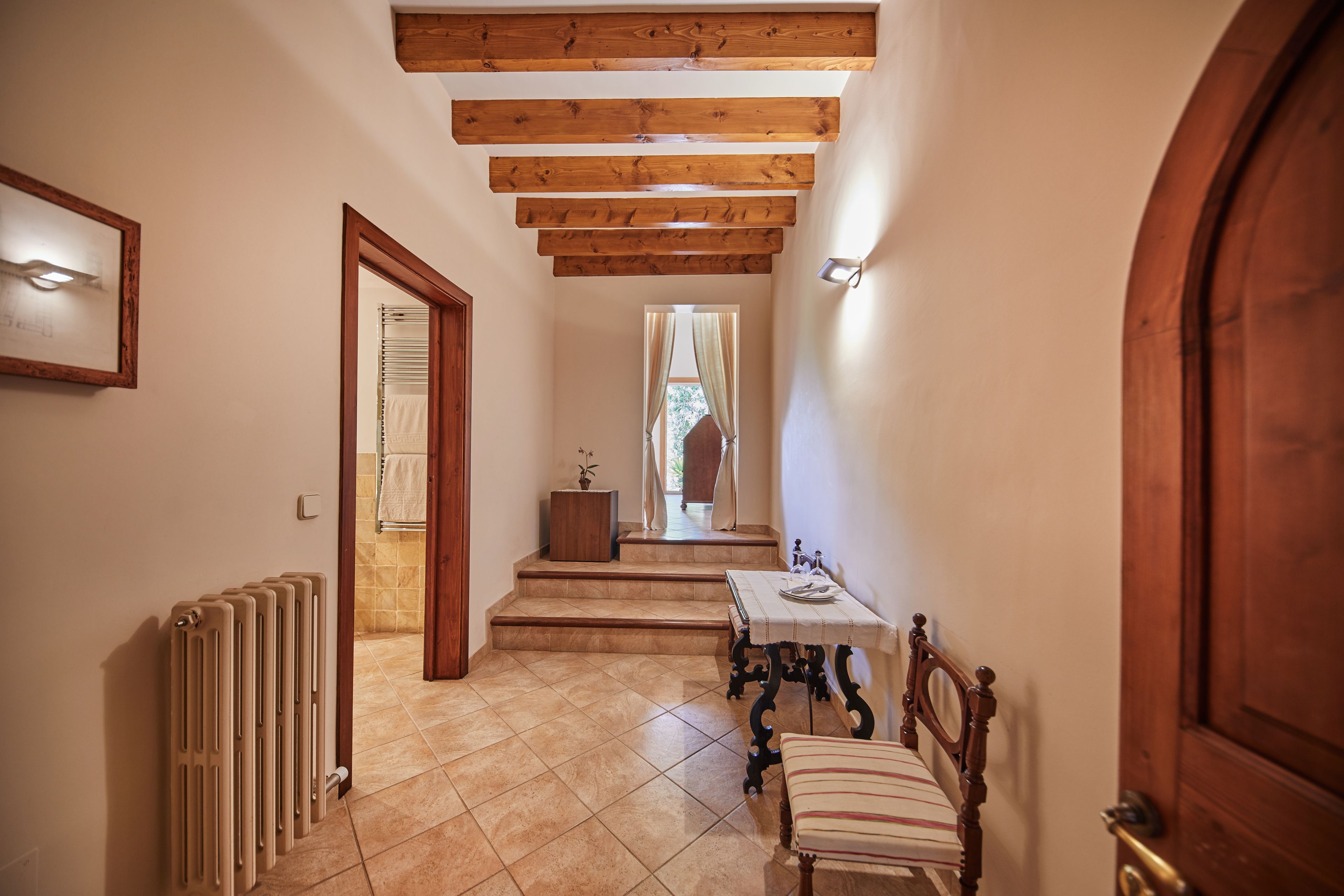 A hallway with a wooden ceiling, a radiator, a table with a chair, and a door.