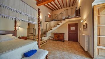 A bedroom with a large bed, a wooden staircase, a dresser, and a radiator.