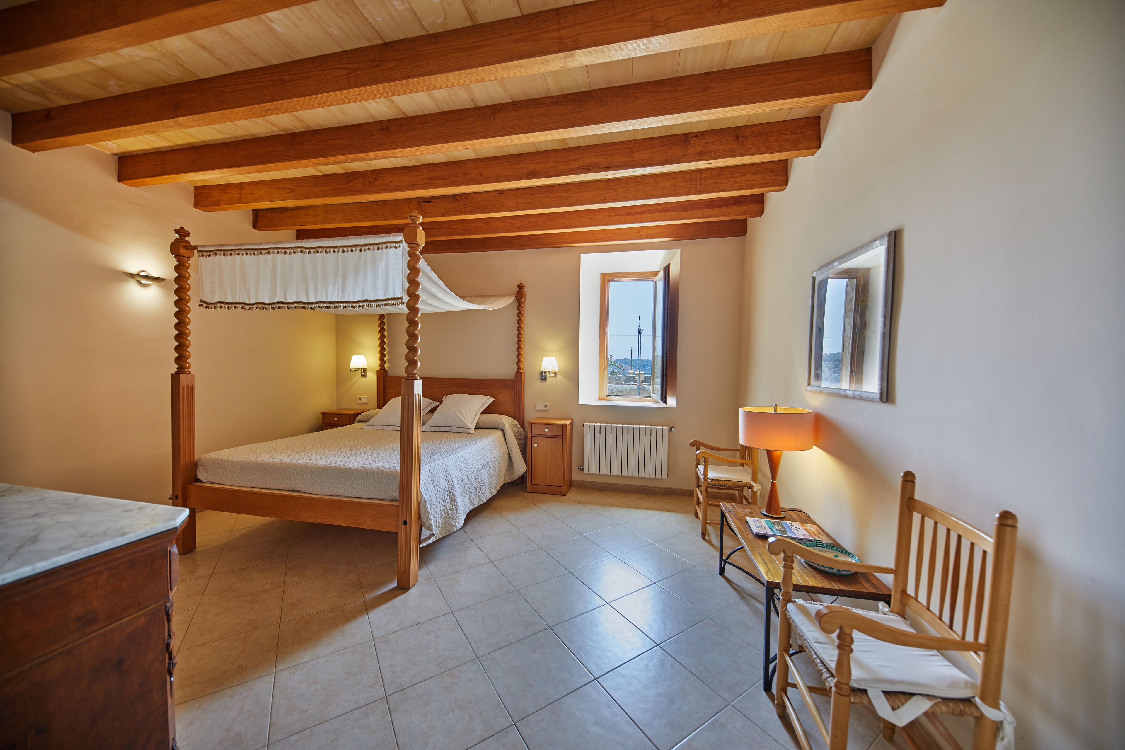 Une chambre à coucher avec un lit à baldaquin, des meubles en bois, un bureau et une fenêtre donnant sur un beau paysage.