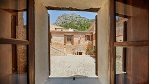 Un bâtiment en pierre doté d’une cour intérieure, de volets en bois et ayant une montagne en toile de fond.