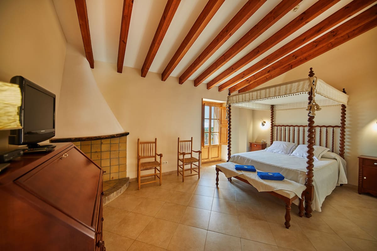 Ein Schlafzimmer mit Himmelbett, Holzbalken an der Decke, einem Fernseher auf einem Schrank und zwei Sesseln.