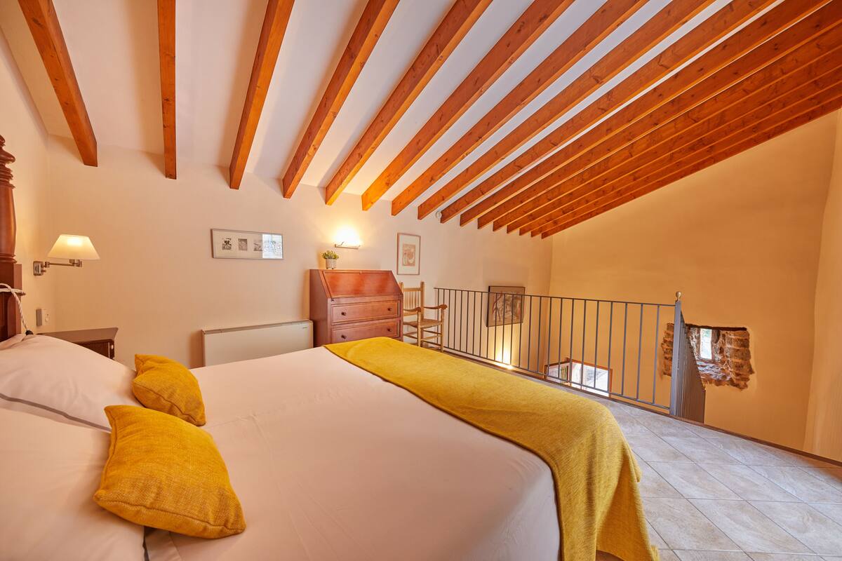 Ein Schlafzimmer mit Holzboden, einem Bett mit gelben Kissen, einem Nachttisch, einer Kommode und einem kleinen Tisch mit Lampe.