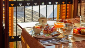 Une table à manger dressée avec des aliments pour le petit-déjeuner, et une vue sur les montagnes par une porte ouverte.