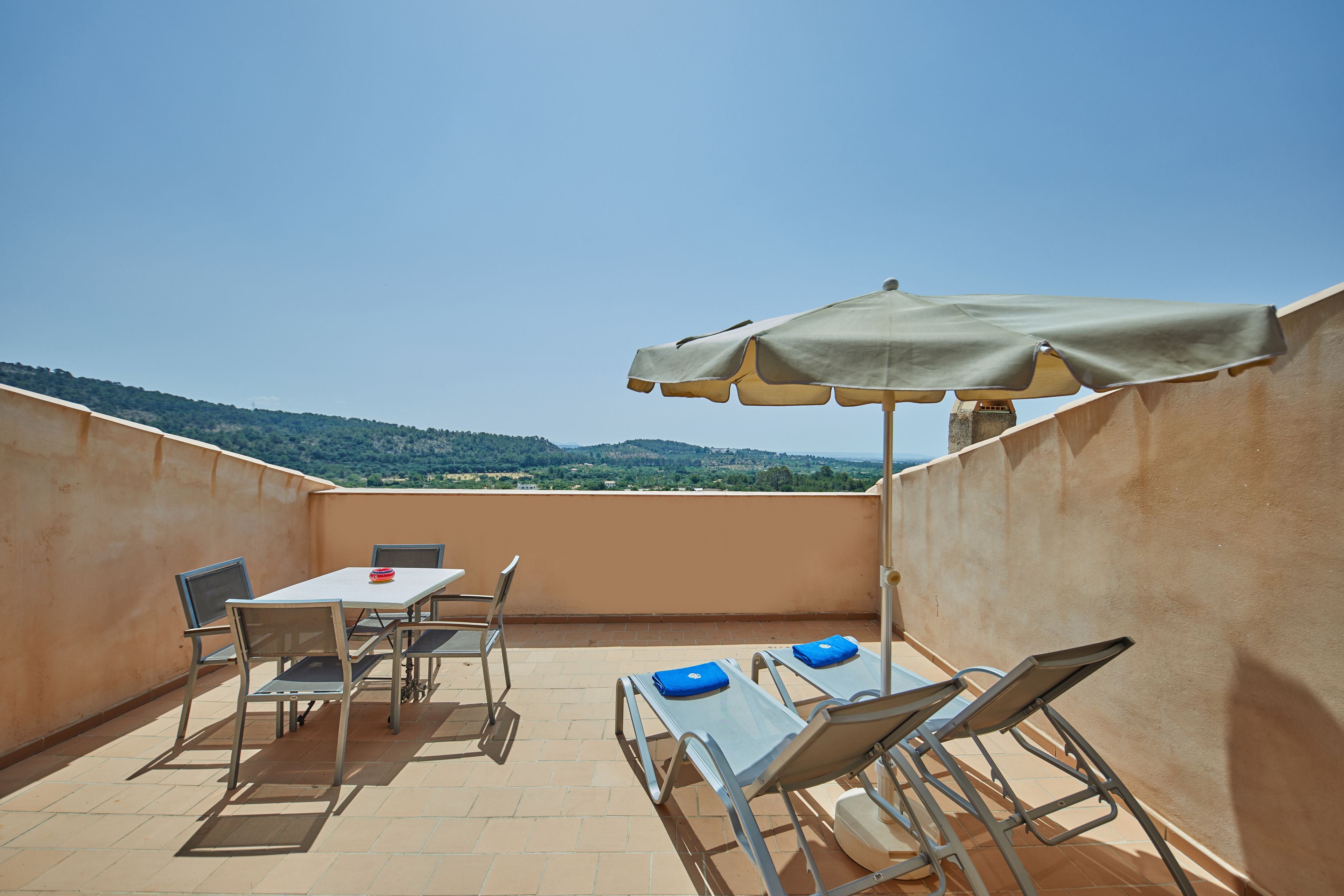 Una terraza en la azotea con una mesa, sillas, una sombrilla y vistas a las colinas.