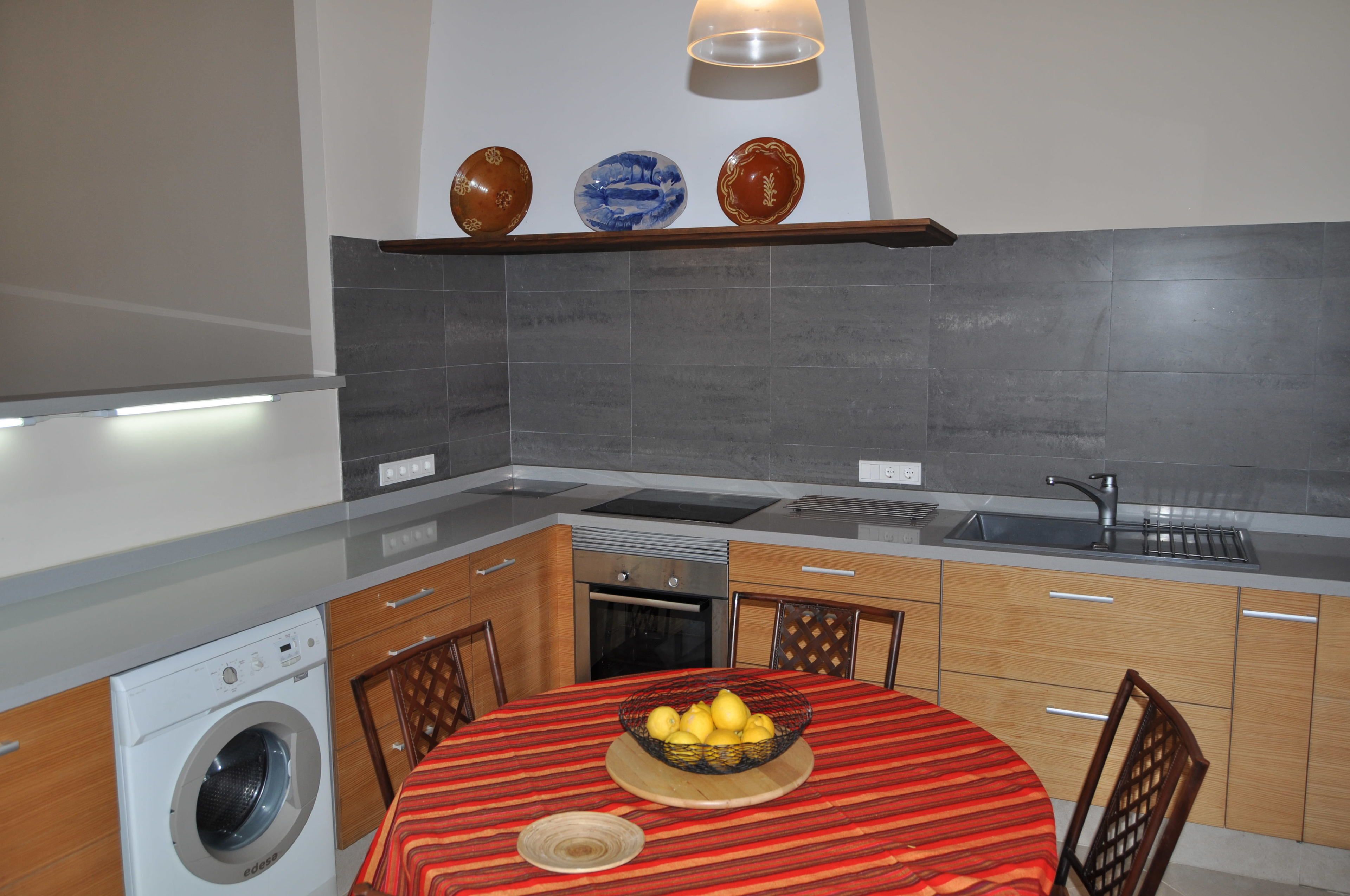 Une cuisine compacte équipée d’un lave-linge, d’un évier et d’un coin repas avec une table dressée pour deux personnes.