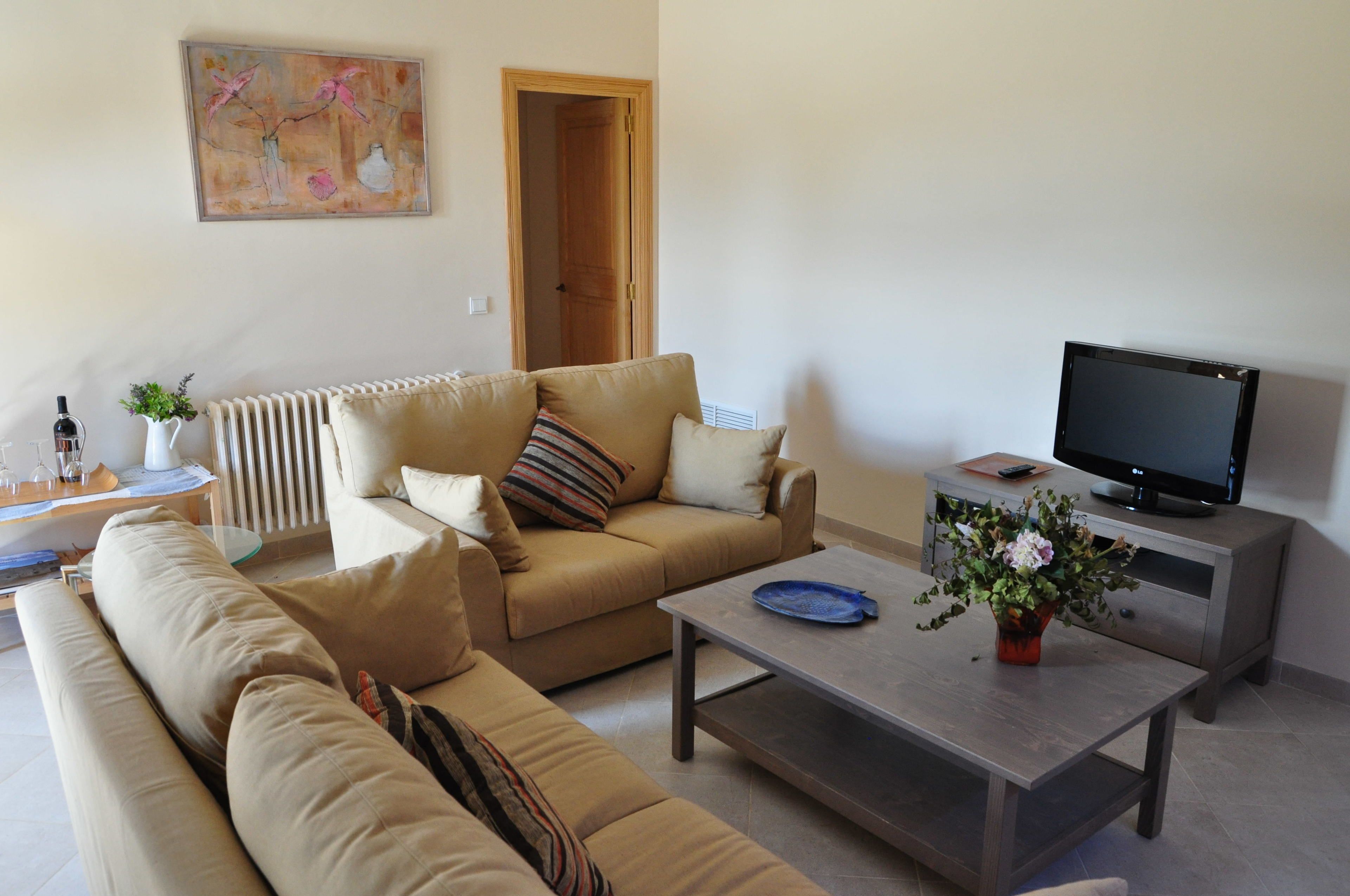 A living room with a beige sofa, a coffee table, a television on a stand, and a door leading to another room.