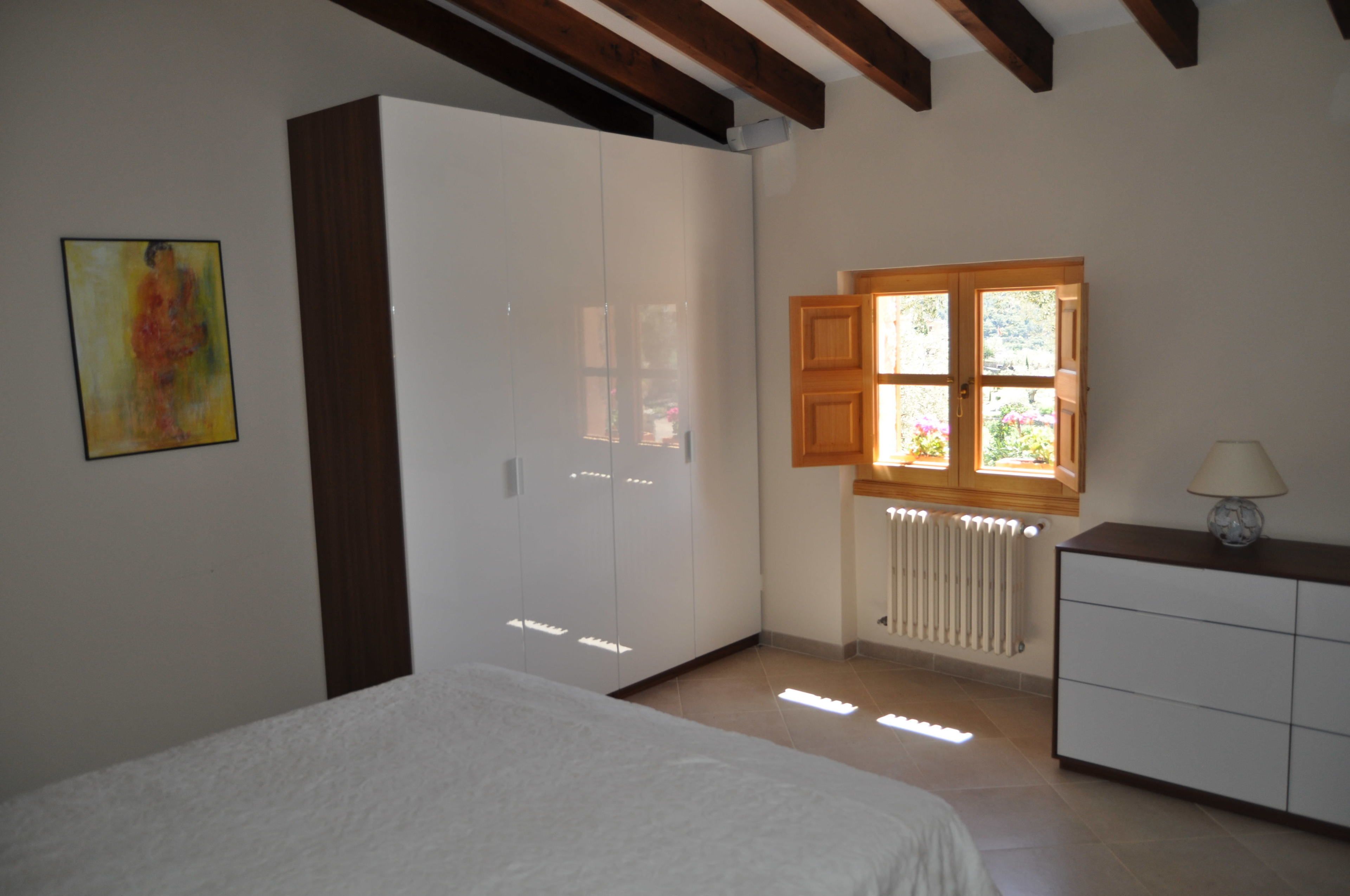 A bedroom with a bed, a wardrobe, a window with shutters, and a radiator.