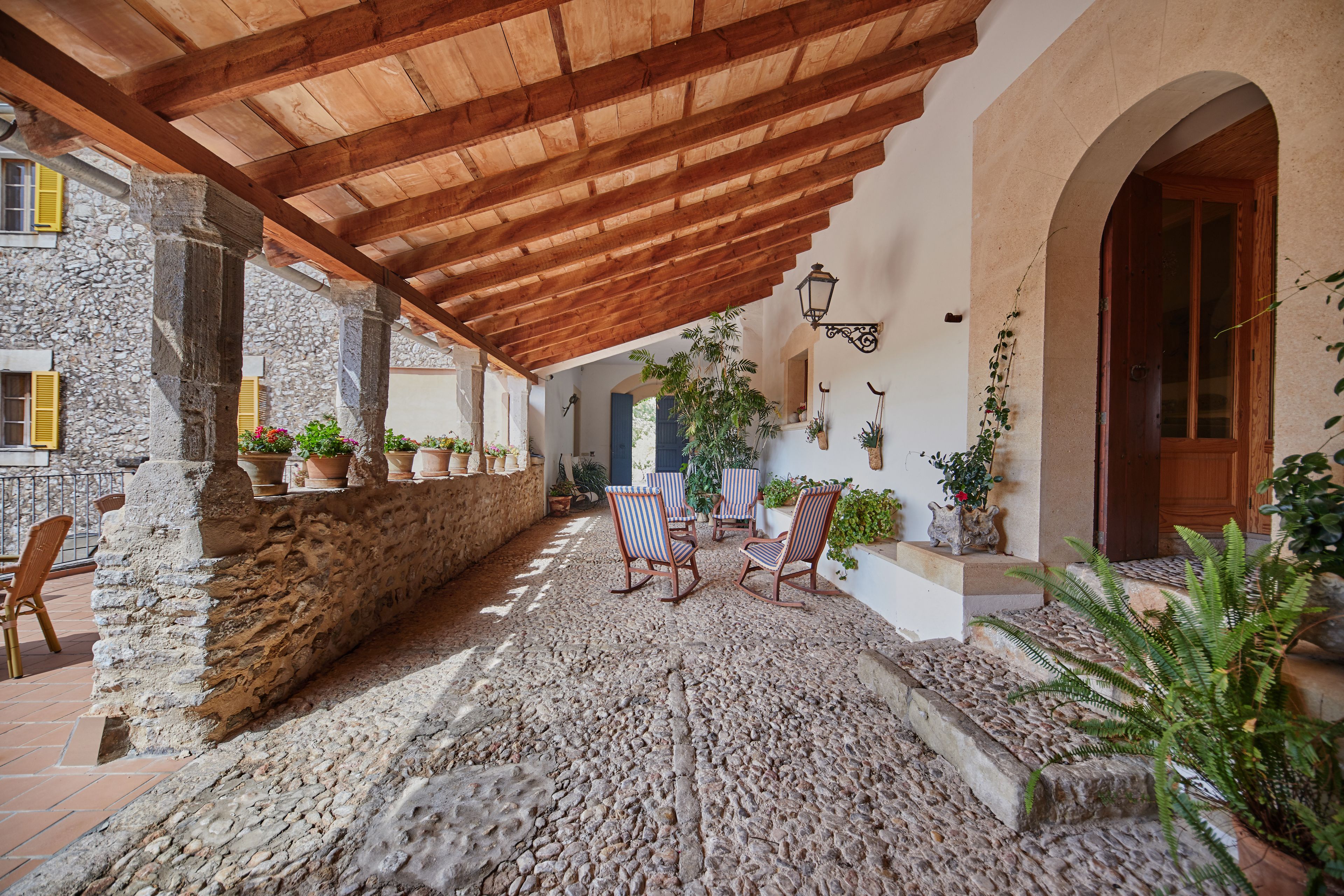A covered outdoor patio with stone walls, wooden beams, and potted plants.