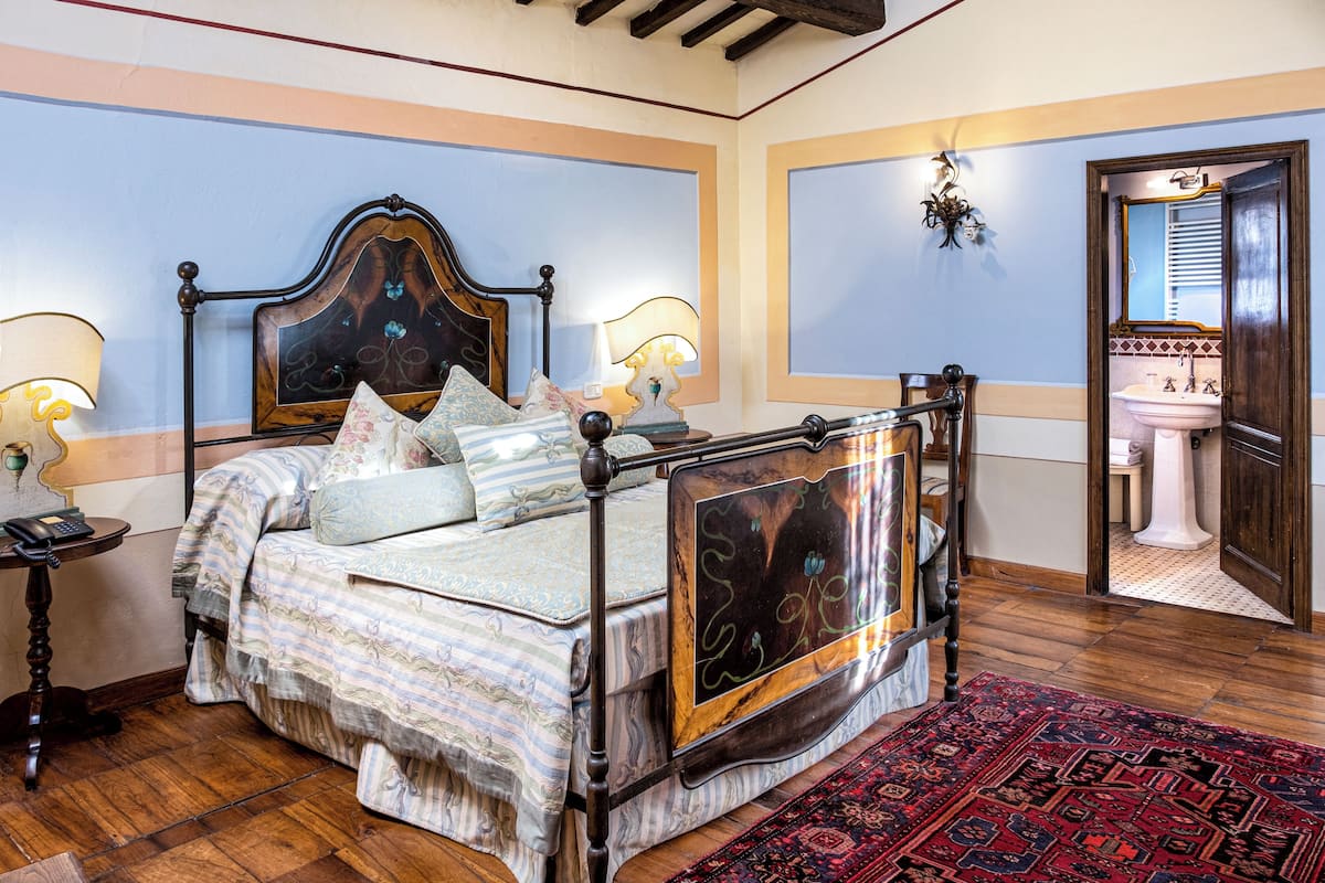 A bedroom with a four-poster bed, a nightstand with a lamp, a large mirror, and a view into the bathroom.