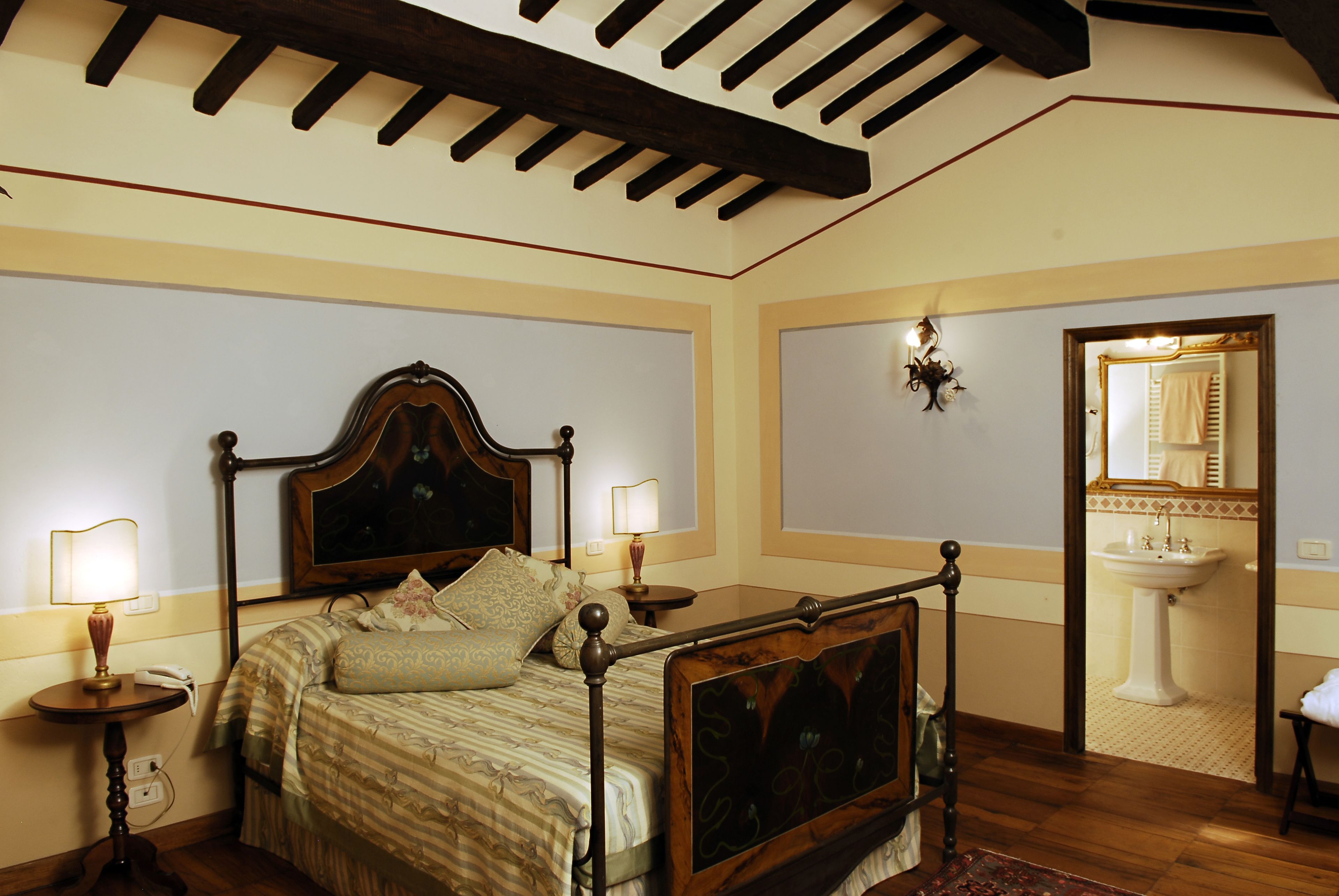 Une chambre à coucher avec un lit en bois, des lampes de chevet, une table de chevet, un miroir et une salle de bain avec un lavabo et un miroir.