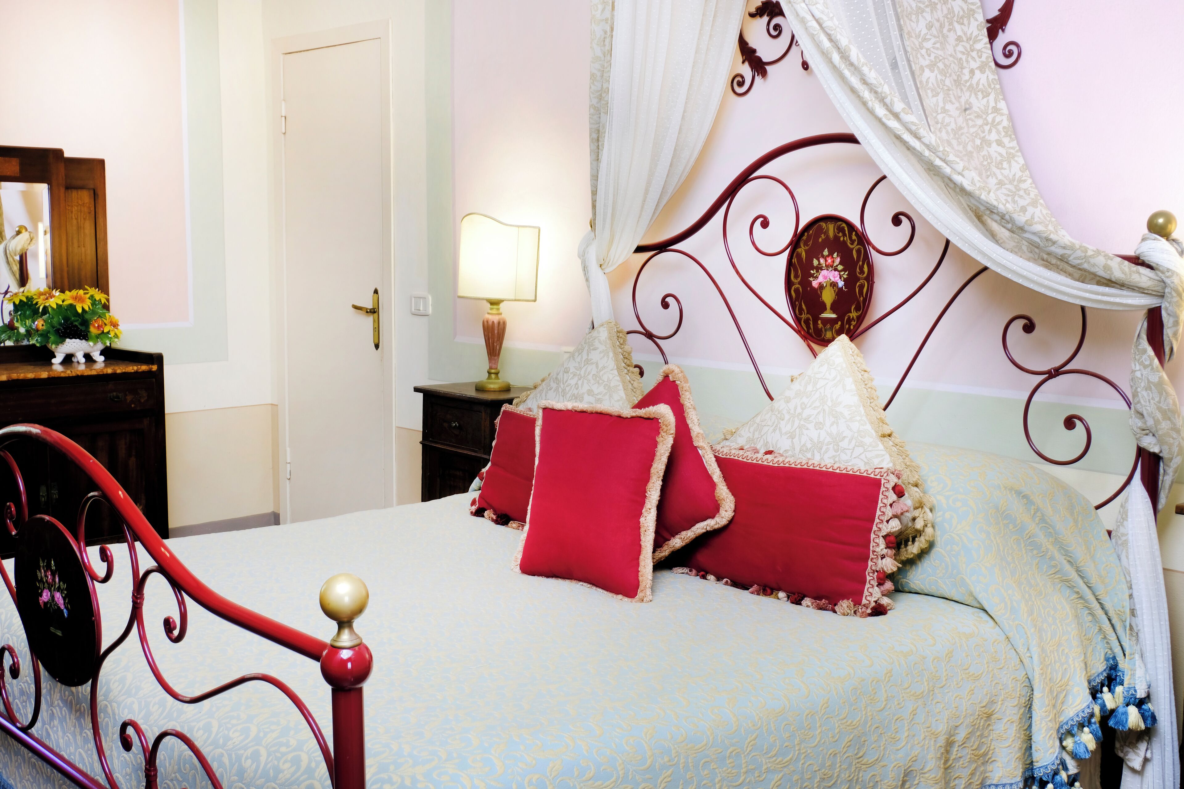 A bedroom with a four-poster bed, a bedside table with a lamp, and a mirror.