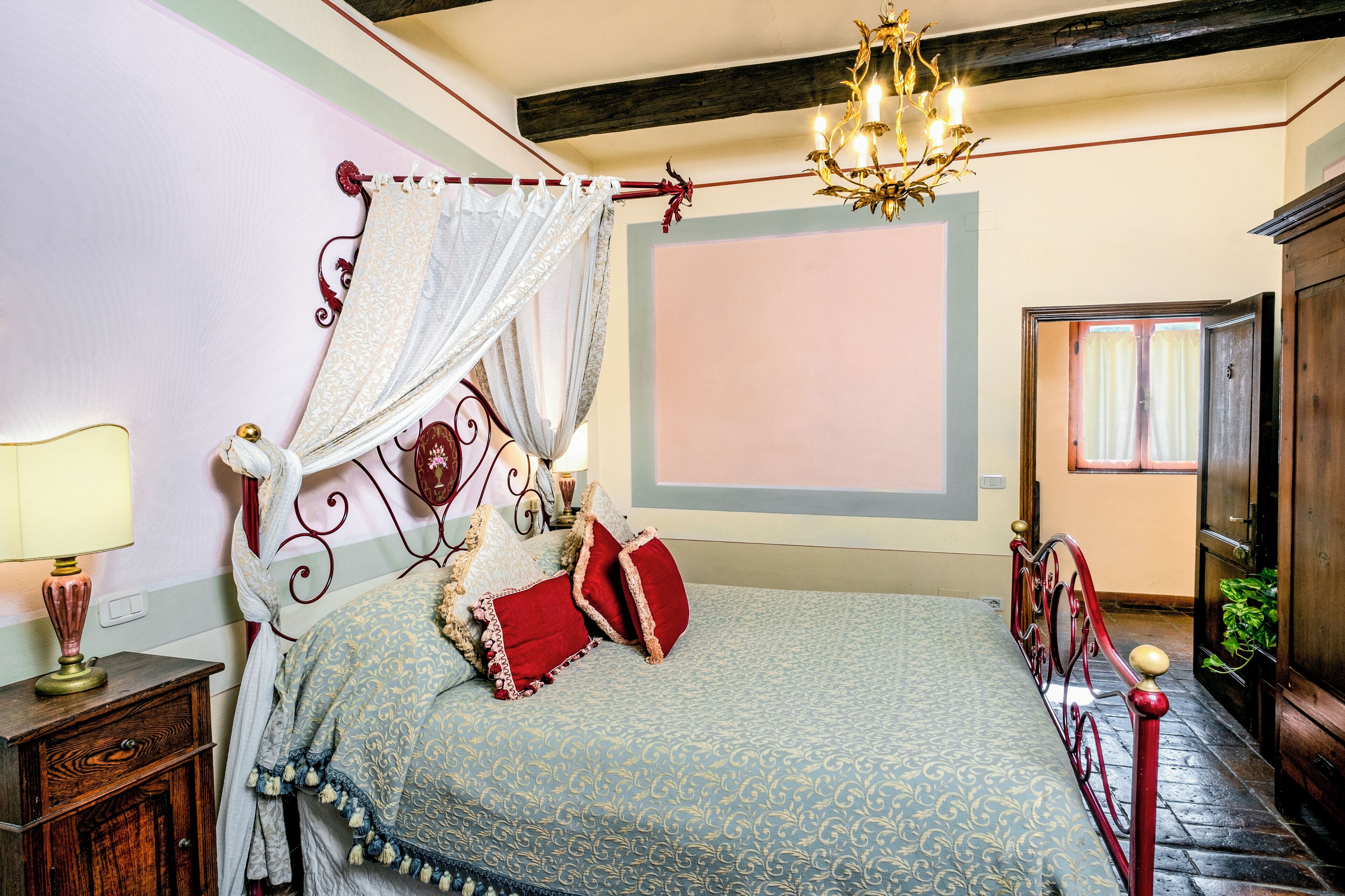 Een slaapkamer met een hemelbed, een kroonluchter en een nachtkastje met een lamp.