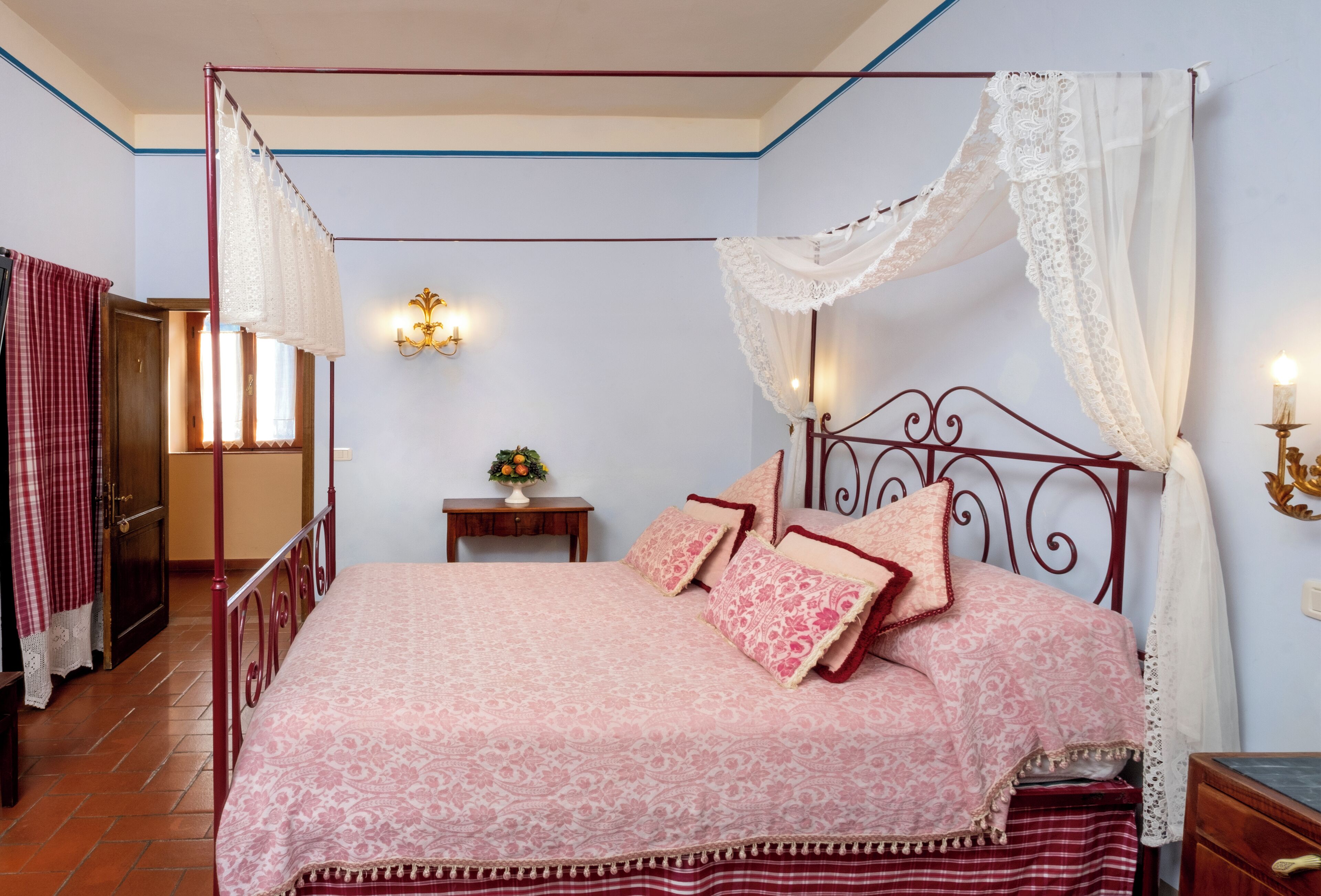 A four-poster bed with a canopy, a bedside table with a lamp, and a nightstand with a candle.